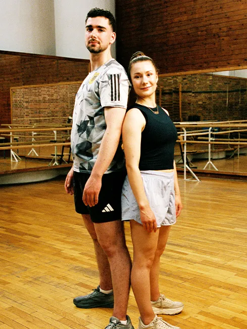 Eiskunstläufer Robert Kunkel und Annika Hocke schauen sich in die Augen beim Tanz auf dem Eis, in dunklen Outfits mit Strasssteinchen und halbtransparenten rötlichen Panelen auf den Oberteilen, mit jeweils einem erhobenen Arm (Foto)