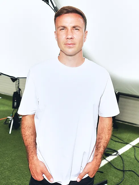 Fußballer Mario Götze im weißen T-Shirt schaut gerade in die Kamera, mit leicht zugekniffenen Augen (Foto)